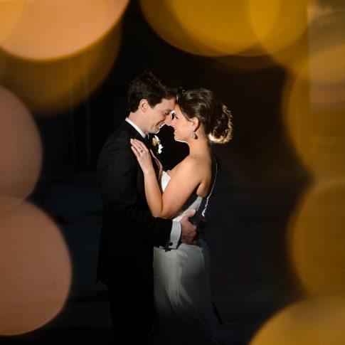 On the rooftop of the Westin Poinsett Hotel, a bride and groom share a happy gaze while the bokeh of the rooftop lights surrounds them.